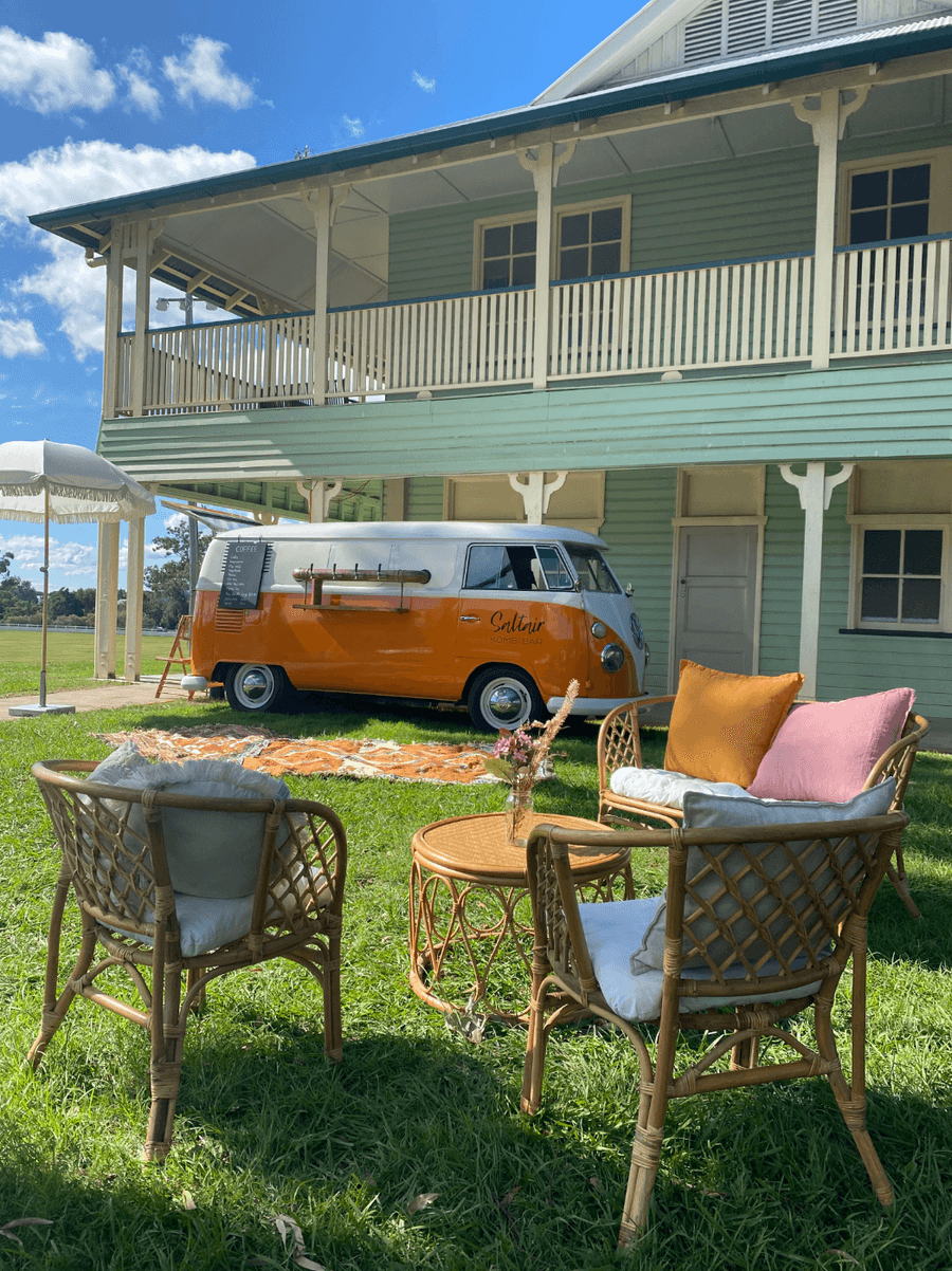 Orange camper van parked on a lawn beside a house, with outdoor chairs